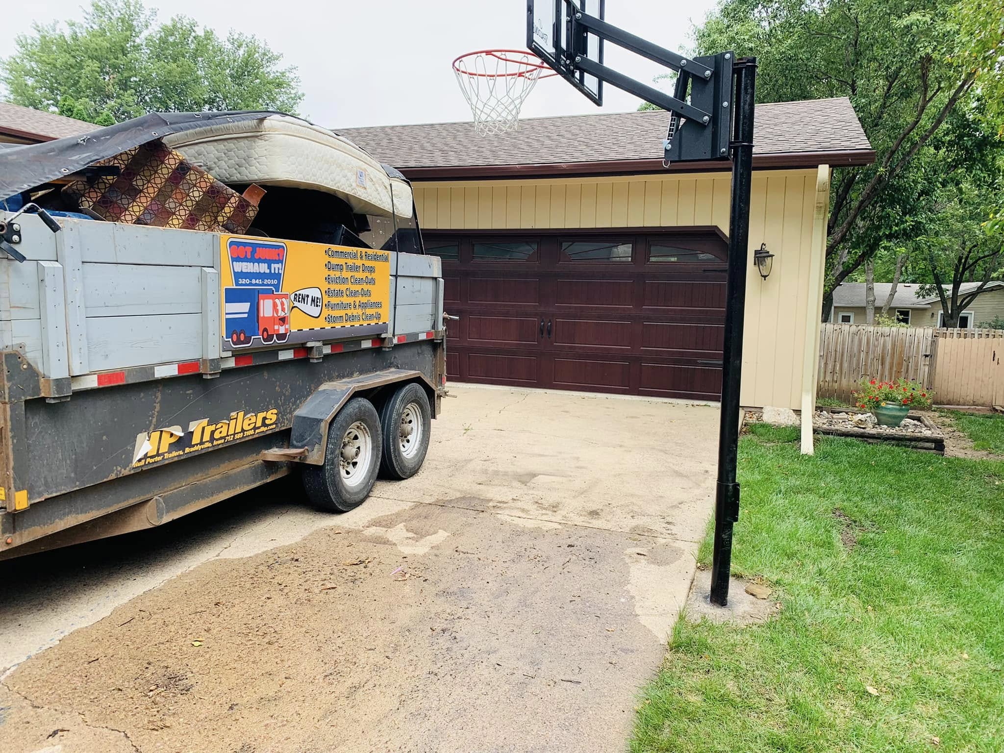 WeHaul roll-off dump trailer parked in a Sioux Falls driveway, branded with the Got Junk WeHaul It logo and 320-841-2010